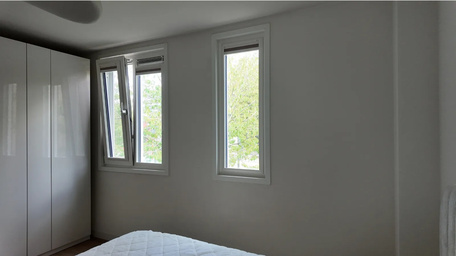 Slaapkamer met egaal gespoten wanden en plafond, zonder rolstructuur, en witte kozijnen rond twee ramen die op het groen uitkijken.