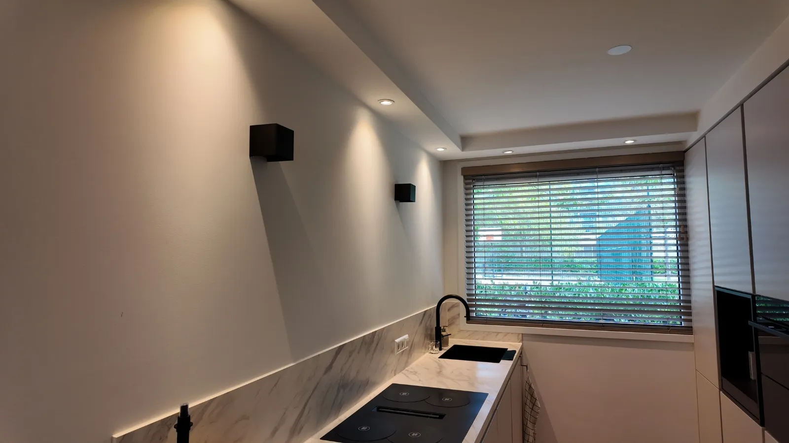 Opgeleverde keuken met egaal afgewerkte wanden en plafond, inbouwspots die het vlak van opzij aanlichten en een strakke aansluiting rond het raamkozijn.