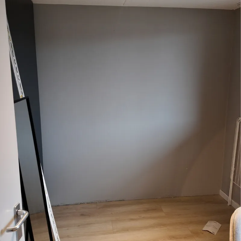 Kinderkamer met een egaal geverfde wand in een zachte grijsblauwe tint, strakke overgang naar de plint